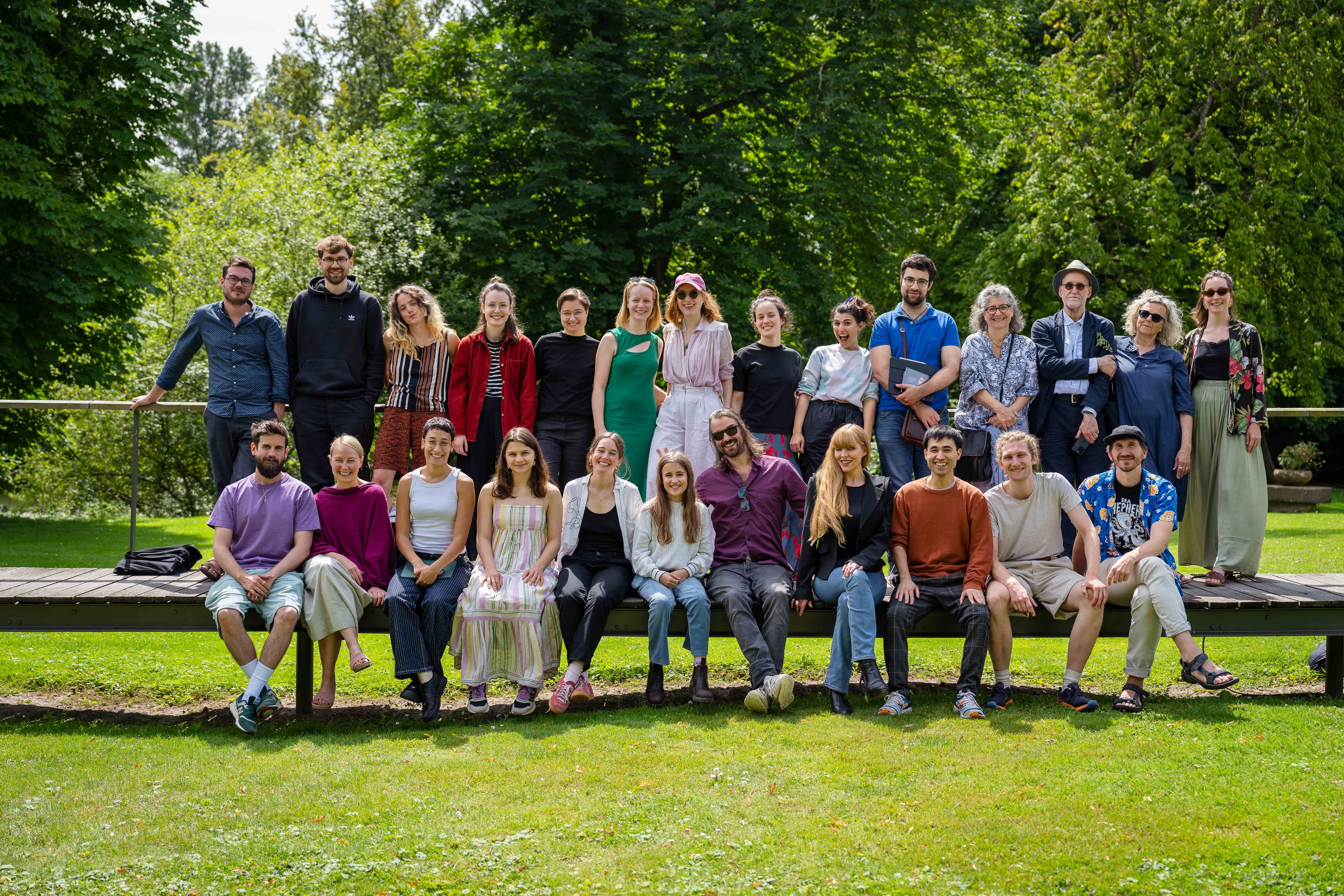 A group of people posing together outdoors on a sunny day, with lush green trees in the background.